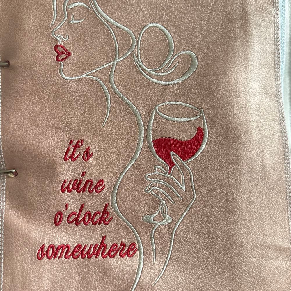 Bestickter Schriftzug mit Silhouette und Weinglas-Motiv auf hellem Leder